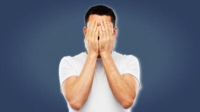 2021/02/Life-Sucks_-Man-in-White-Shirt-Holding-Hands-Over-Face-Blank-Background.jpg